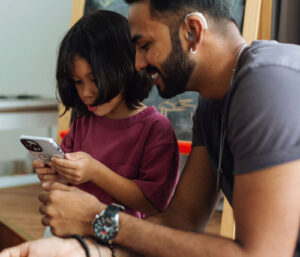 Man with a hearing aid and his child looking at a phone app